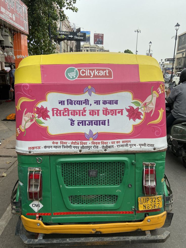 Branded auto rickshaw with full hood advertising at a Delhi Metro station exit in Lajpat Nagar during evening commuter rush